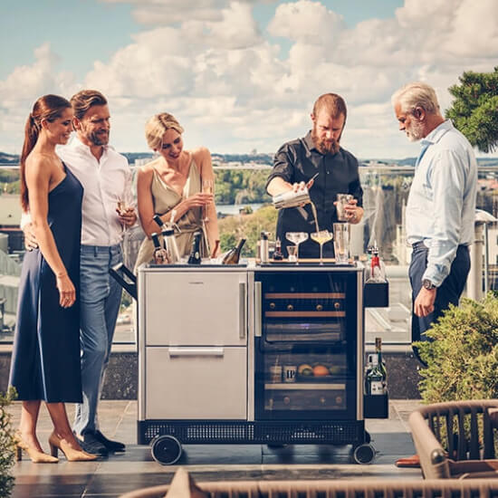 barman uses the dometic mobar to prepare cocktails at a terrace party with people around